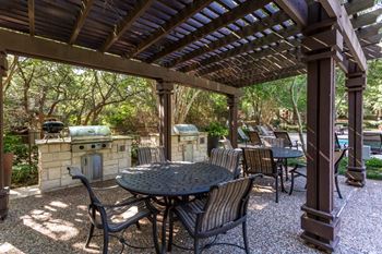 An outdoor kitchen and dining area under a pergola with trees in the background